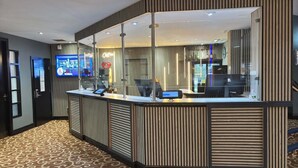 A reception desk with a digital screen, a glass partition, and a patterned carpet. - Britannia Hotel Manchester Airport (Manchester)