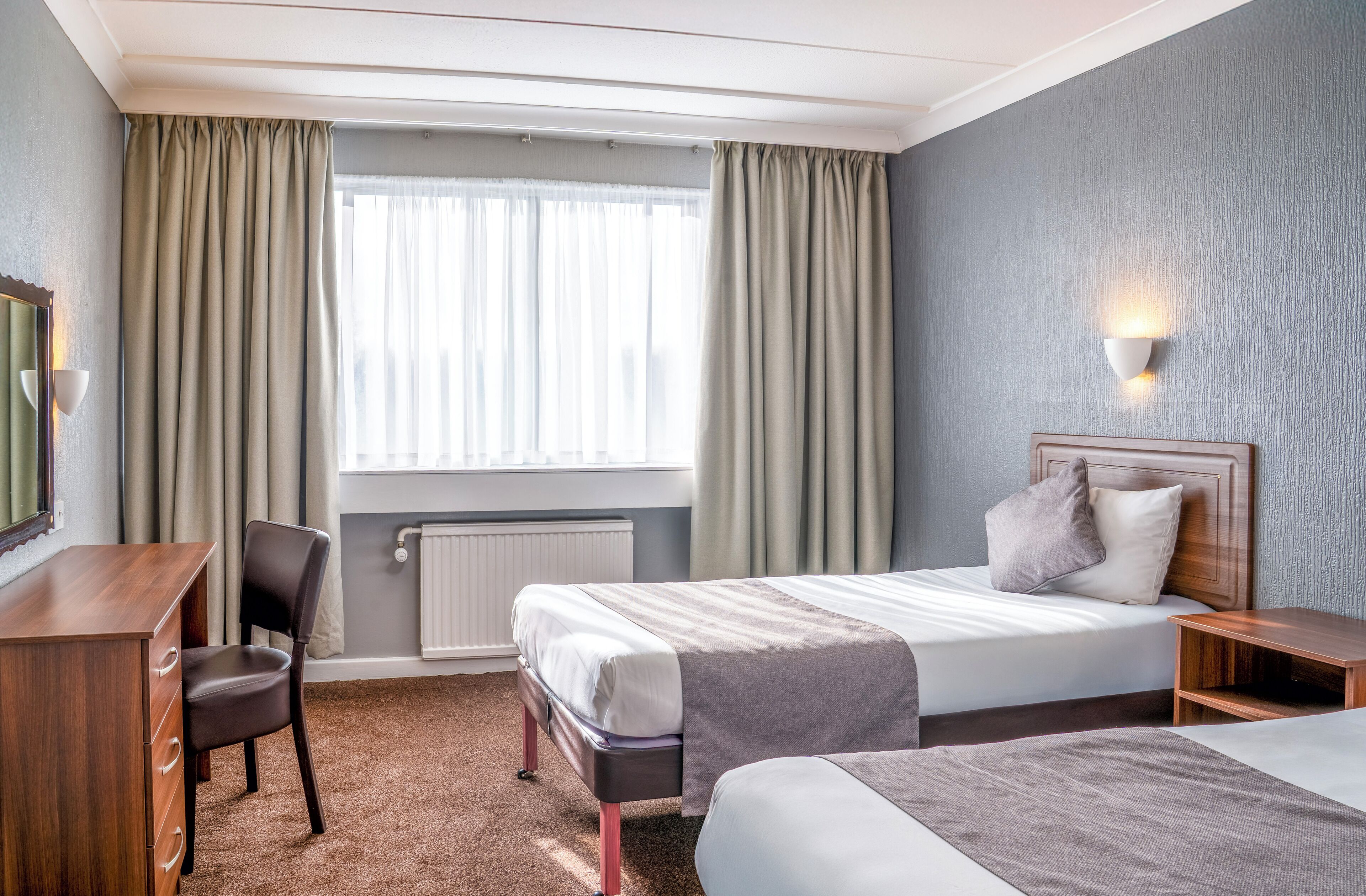 A hotel room with a bed, a desk, a chair, and a nightstand.
