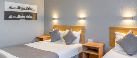 A hotel room with two beds, a cityscape artwork on the wall, and two wall-mounted lights.