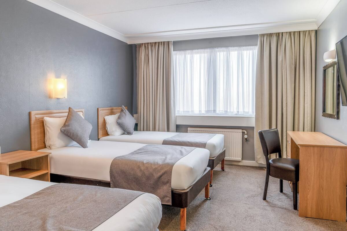 A hotel room with two beds, a desk, a chair, a TV, and a window with curtains.