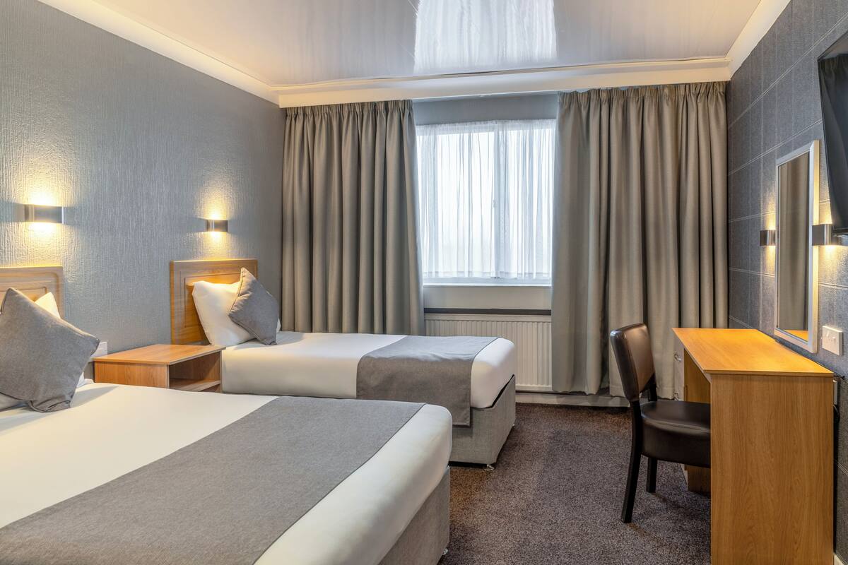 A hotel room with two beds, a desk, a chair, and a large window with curtains.