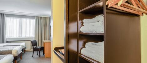 Una habitación de hotel con dos camas, un escritorio, una silla y un armario con ropa colgada.