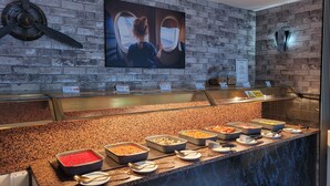 A buffet area with various food options, a brick wall, and a television screen displaying a person looking out a window. - Britannia Hotel Manchester Airport (Manchester)