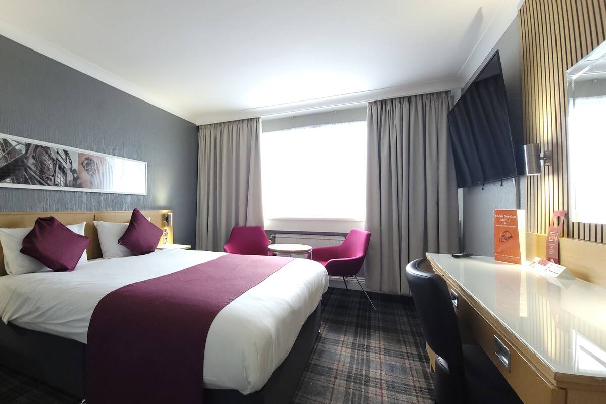 A hotel room with a bed, a desk, a chair, and a window with curtains.