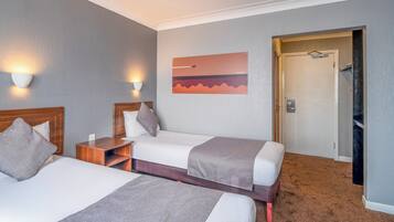 Habitación de hotel con dos camas, una mesita de noche, una lámpara en la pared y una puerta que da a un armario.