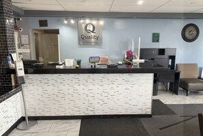 A hotel reception desk with a 'Quality by Choice Hotels' sign, a clock, and a digital screen.