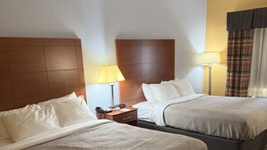 Habitación de hotel con dos camas, una mesita de noche con lámpara y cabecera.