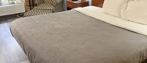 Una habitación de hotel con una cama grande, una mesita de noche con lámpara, una silla y una ventana con cortinas.