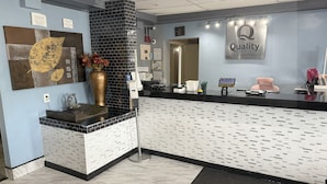 Una zona de recepción con pared de baldosas blanco y negro, una gran obra de arte con pan de oro, un jarrón con flores y un letrero de 'Quality by Choice Hotels'.