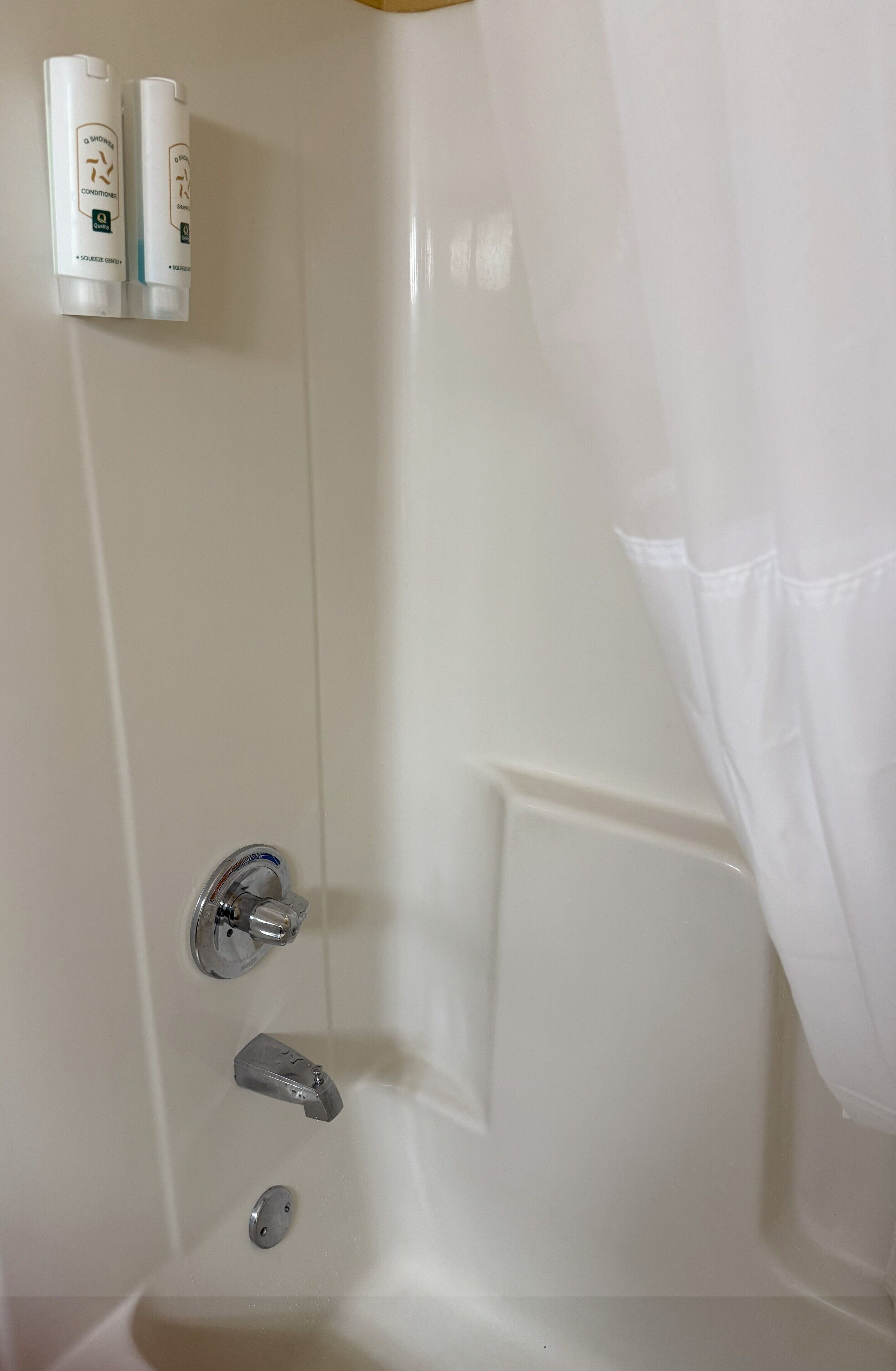 Une baignoire blanche avec un rideau de douche, un robinet et deux bouteilles de shampoing sur une étagère.