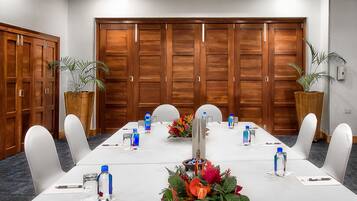 Un salón de conferencias con una larga mesa, sillas blancas y botellas de agua.