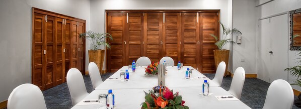 Un salón de conferencias con una larga mesa, sillas blancas y botellas de agua.