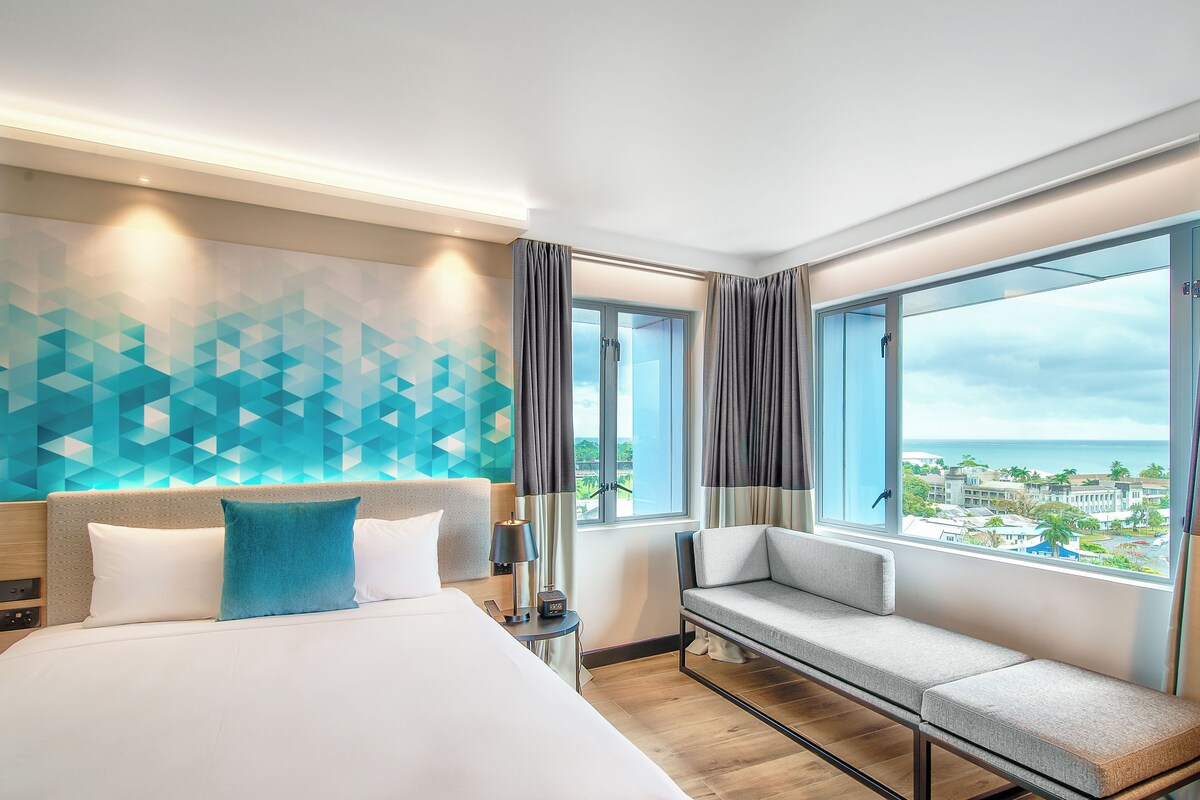 A modern hotel room with a large bed, a sofa, and a view of the city.
