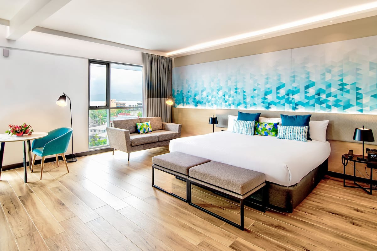 A modern hotel room with a large bed, a desk, a chair, and a view of the city.