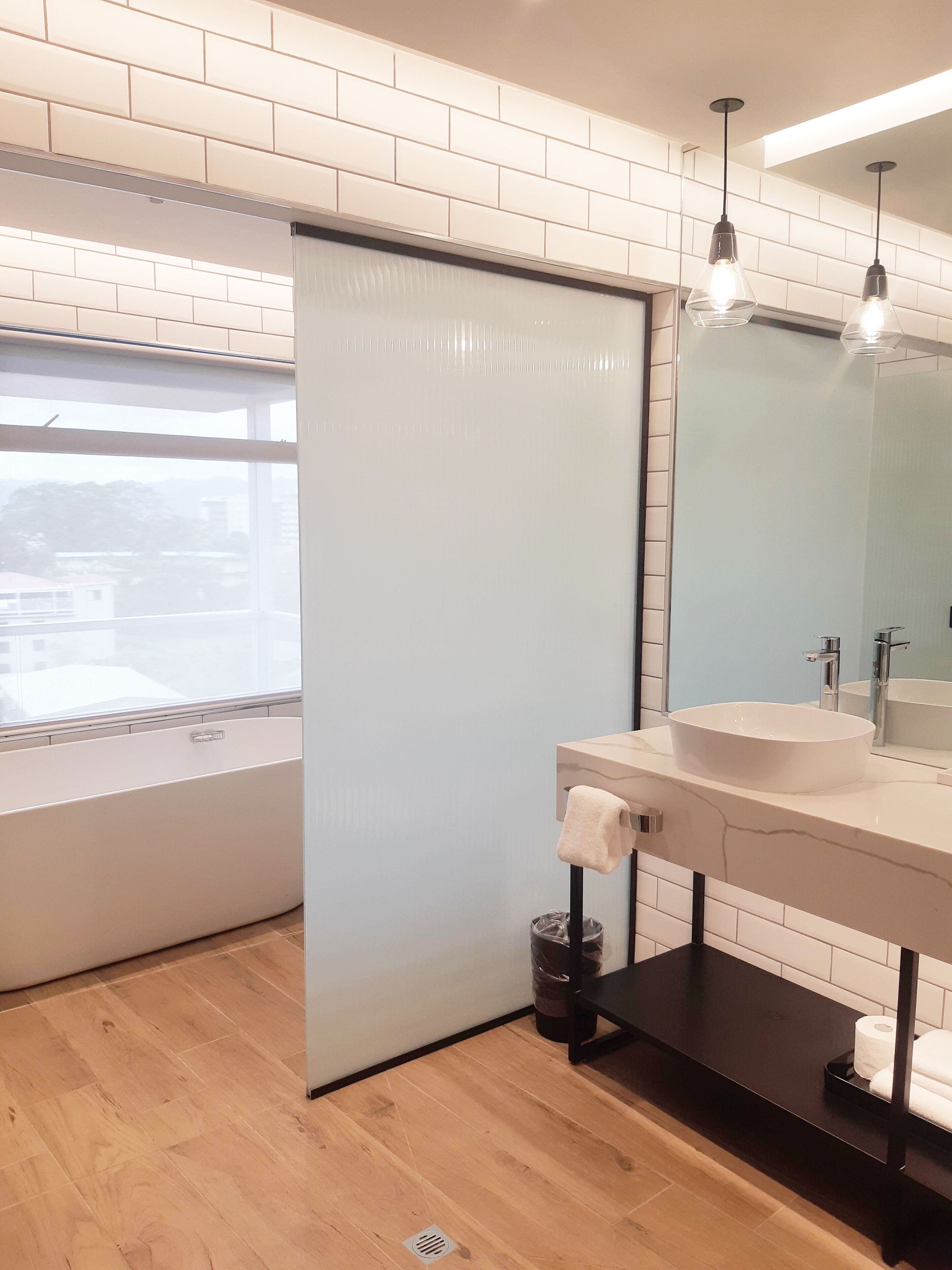 Une salle de bain moderne avec une grande fenêtre, un lavabo blanc et une étagère noire.