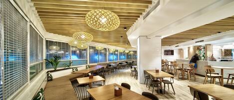 A modern restaurant with wooden ceiling slats, hanging spherical light fixtures, and a variety of seating options including tables and benches.