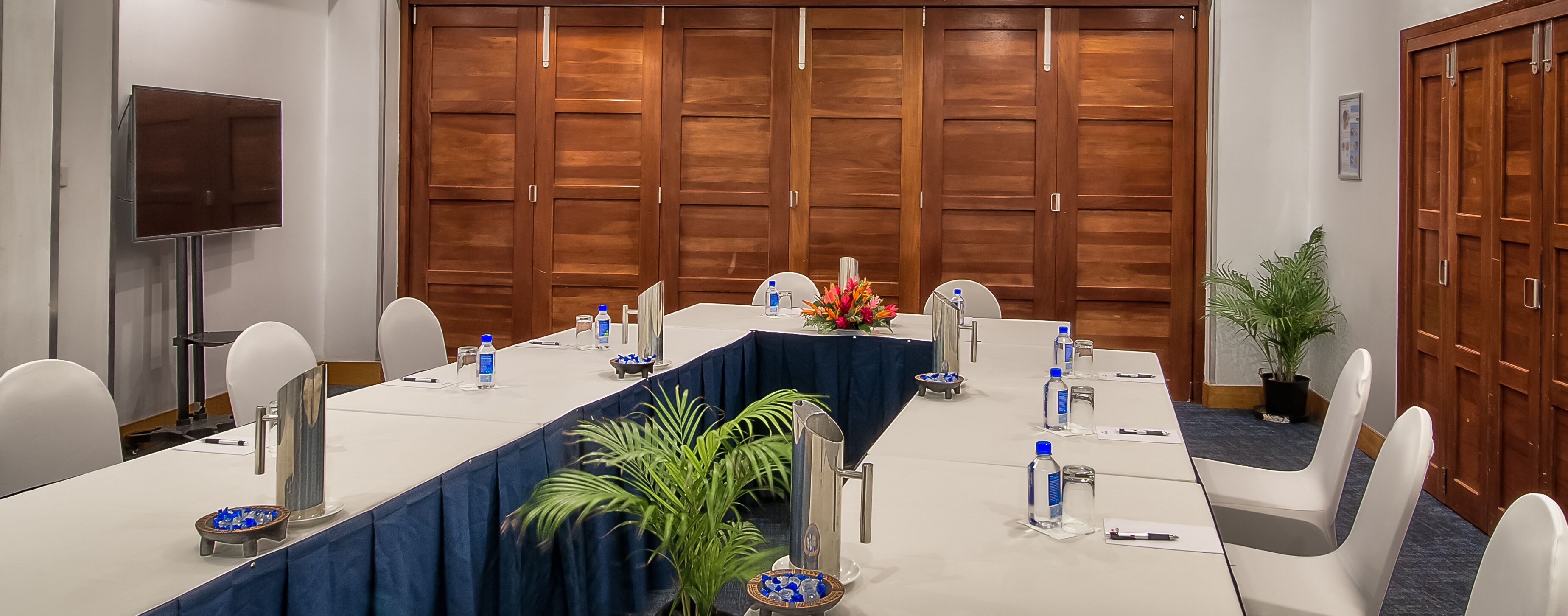 A conference room with a long table, chairs, a TV, and wooden doors.