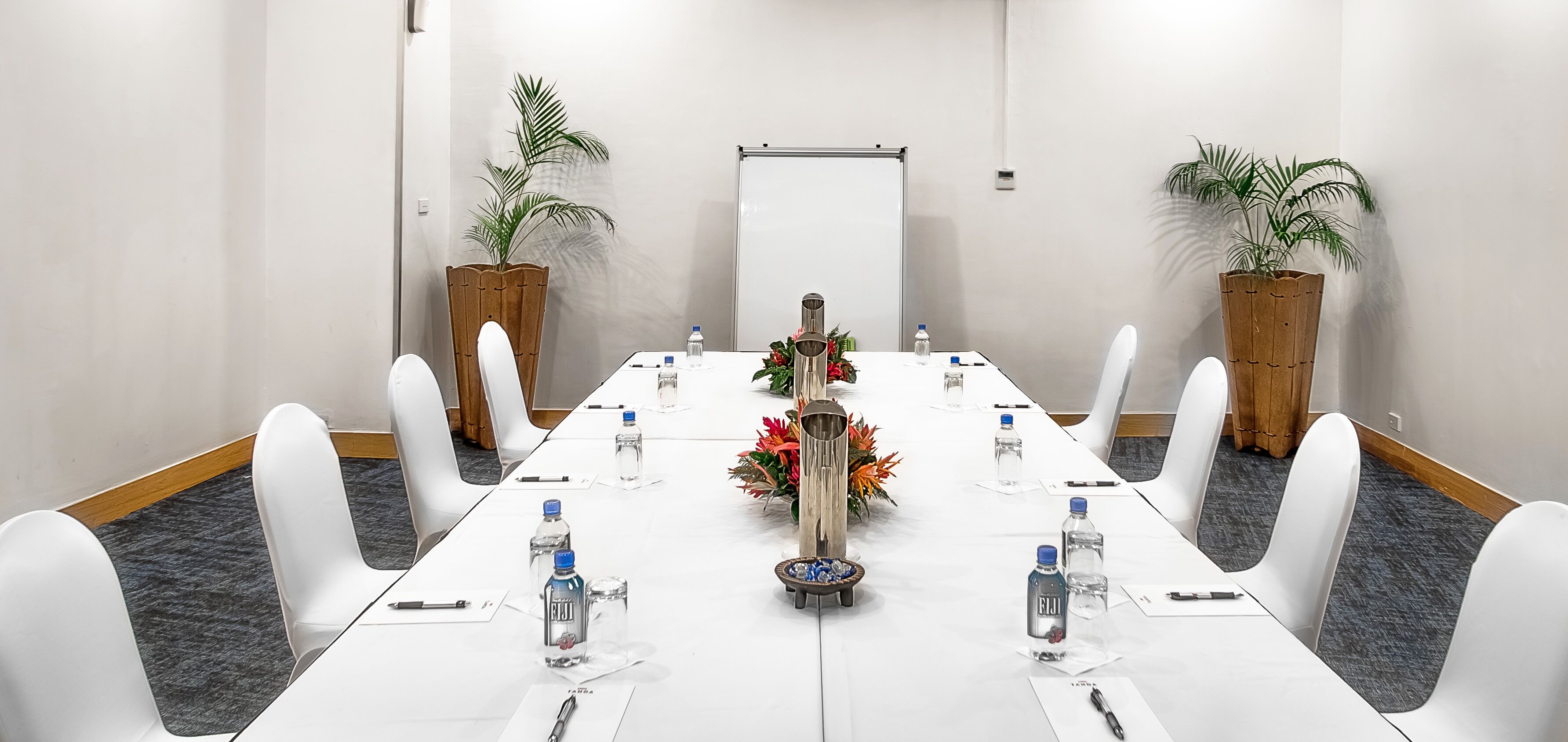 A conference room with a long table, white chairs, water bottles, and a whiteboard.