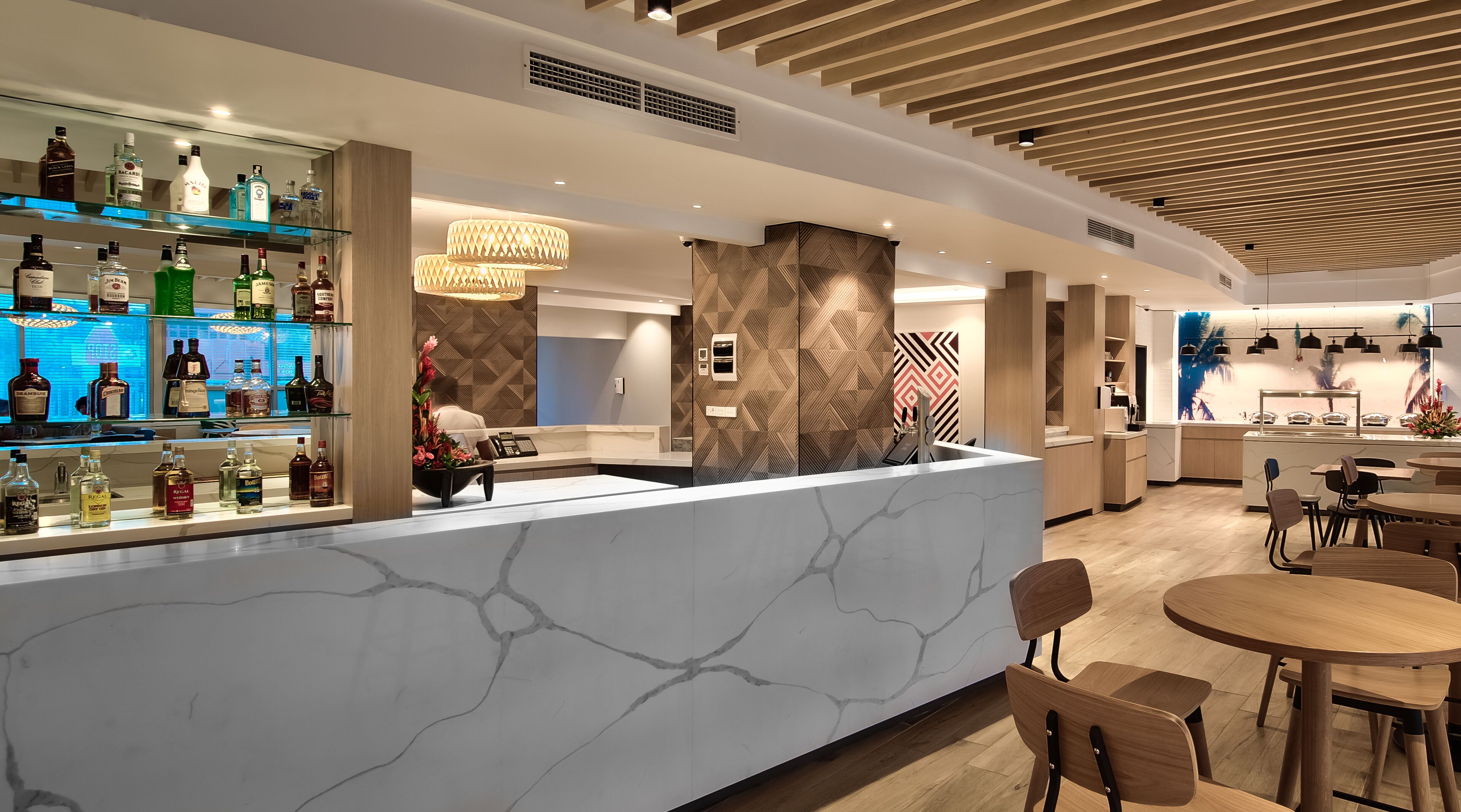Un moderno bar con una barra de mármol, varias botellas de licor y un arreglo floral decorativo.