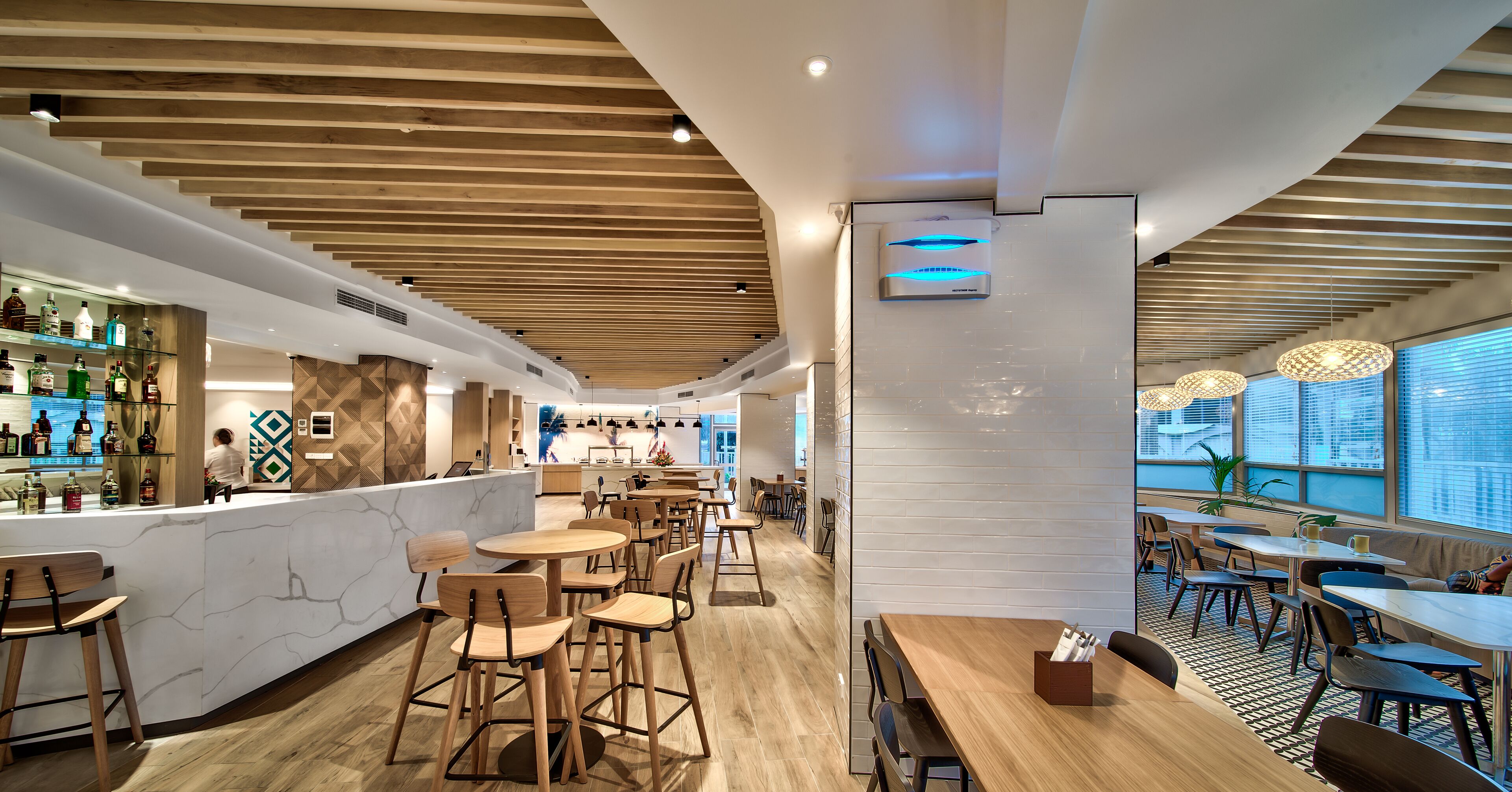 Un restaurante moderno con vigas de madera en el techo, una zona de bar con botellas de licor y diferentes disposiciones de asientos.