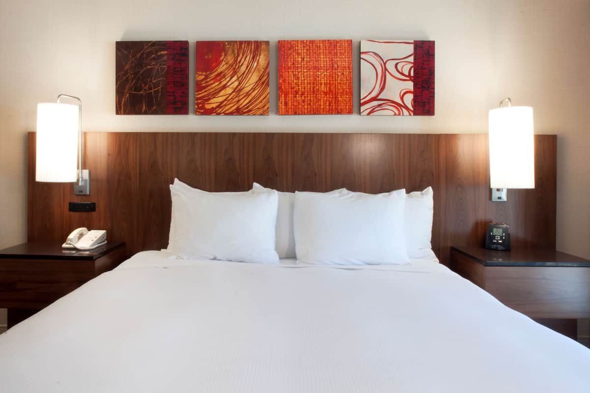 A hotel room with a large bed, two bedside tables, a phone, a clock, and four abstract paintings on the wall.