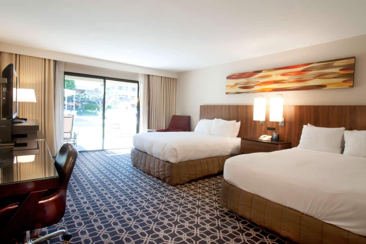 A hotel room with two beds, a desk, a chair, and a large window.