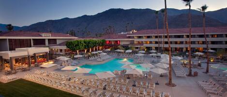 A resort with a swimming pool, lounge chairs, and palm trees.