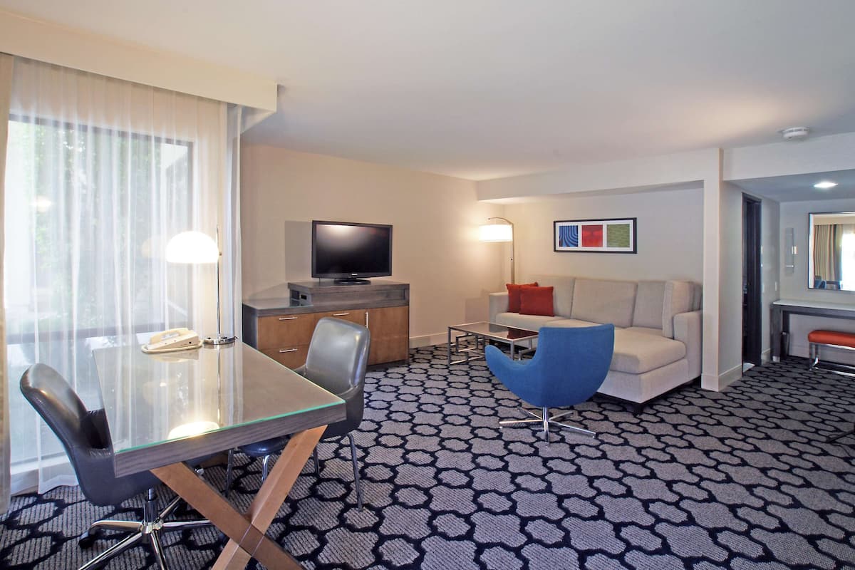 A hotel room with a glass dining table, a sofa, a TV, and a patterned carpet.