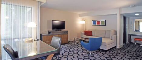 A hotel room with a glass dining table, a sofa, a TV, and a patterned carpet.