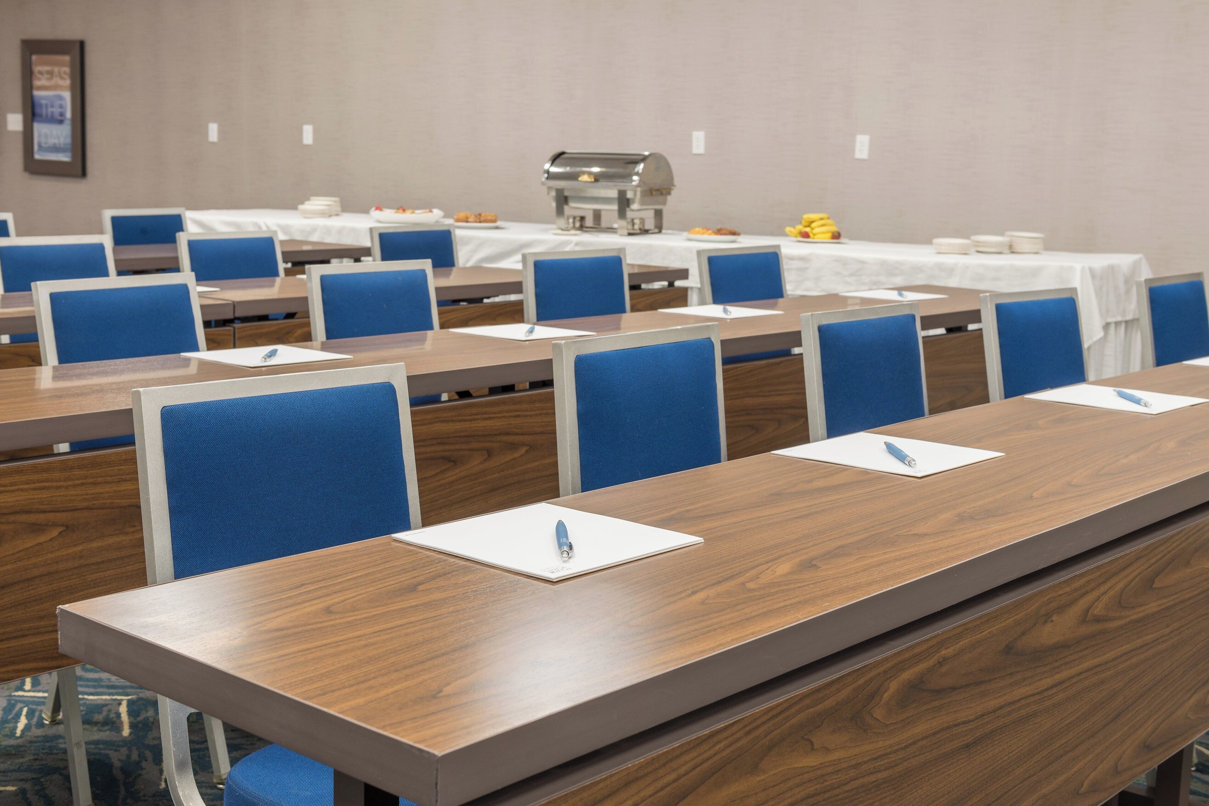 A conference room with long tables, blue chairs, and a buffet area in the background.