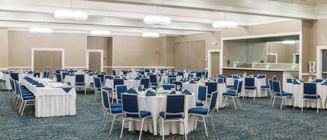 Une vaste salle de banquet avec des rangées de tables rondes et des chaises bleues, un grand miroir et un sol recouvert de moquette.