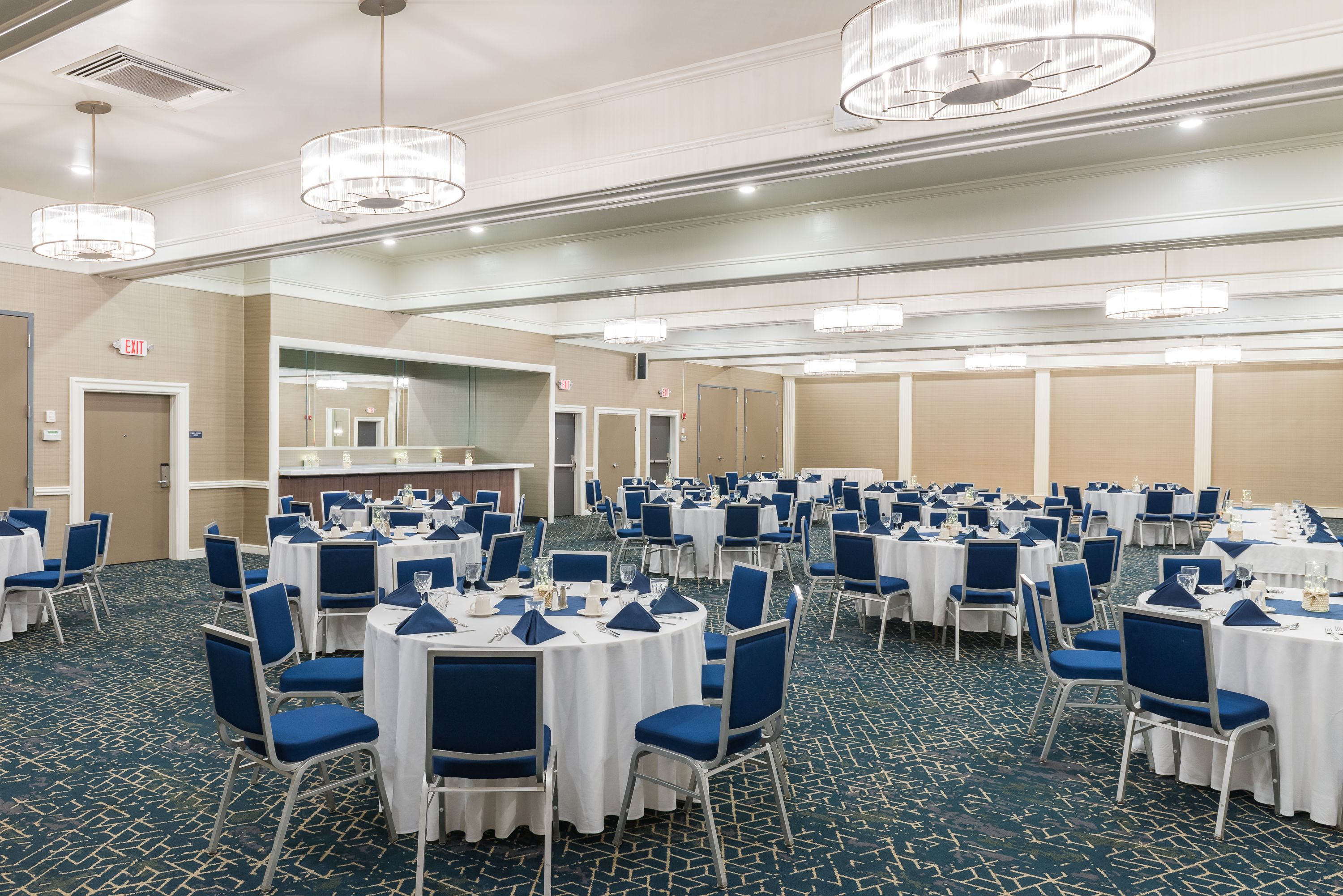 Un salón de banquetes con mesas redondas, sillas azules y manteles blancos.