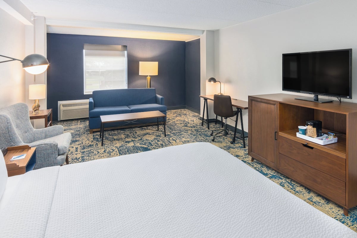 Habitación de hotel con una cama grande, un sofá azul, un escritorio, un televisor y un armario de madera.