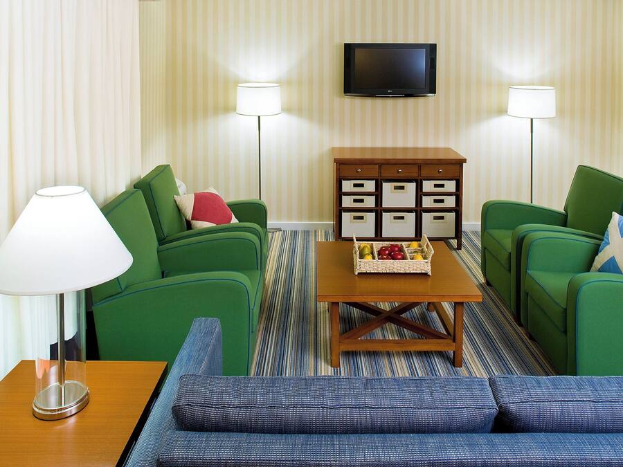 Een hotelkamer met twee groene banken, een houten bijzettafeltje met fruit, een televisie en twee vloerlampen.
