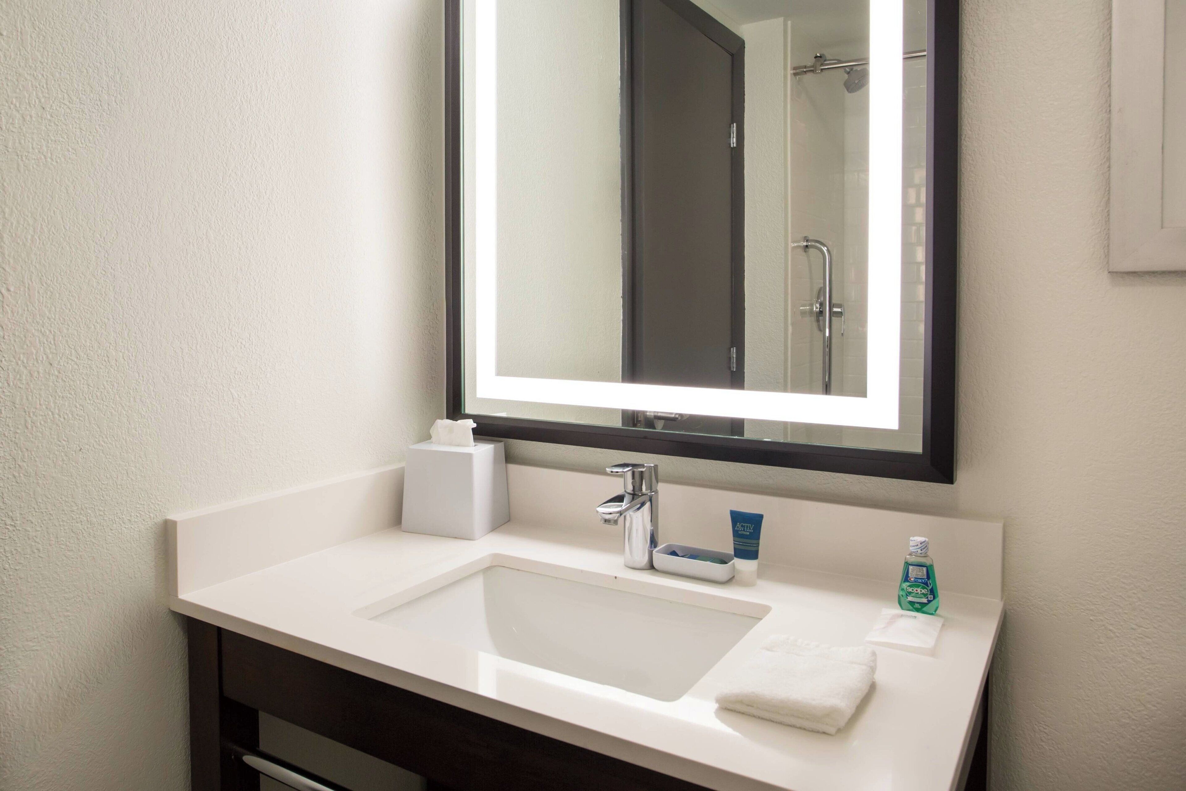 A bathroom with a white sink, a mirror, a towel, and a bottle of hand soap.