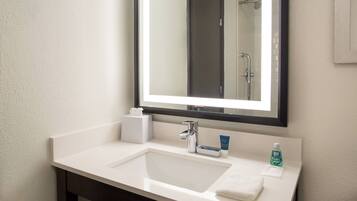 A bathroom with a white sink, a mirror, a towel, and a bottle of hand soap.