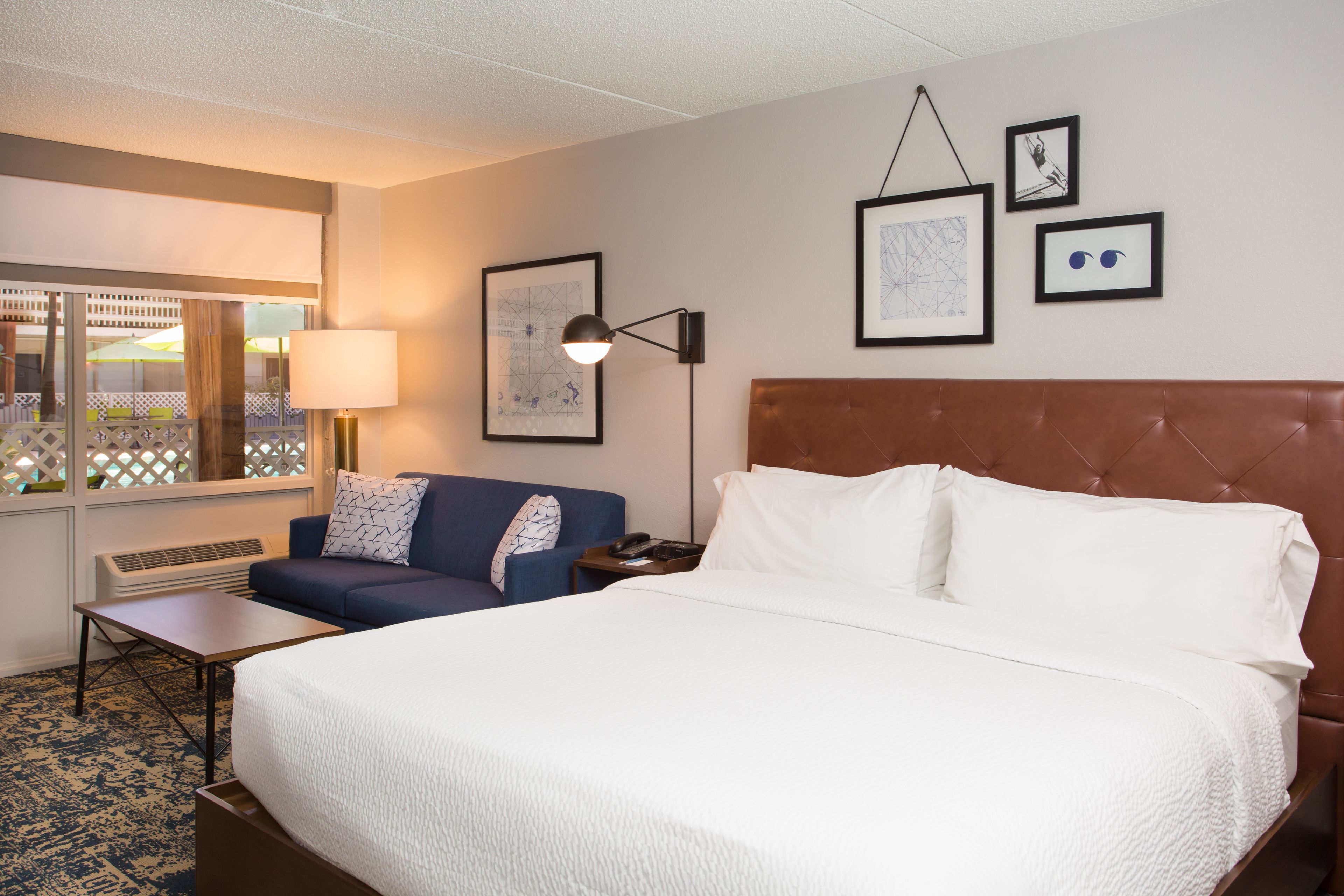 A hotel room with a large bed, a sofa, a desk, and a window with a view of the outside.