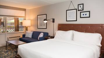 A hotel room with a large bed, a sofa, a desk, and a window with a view of the outside.