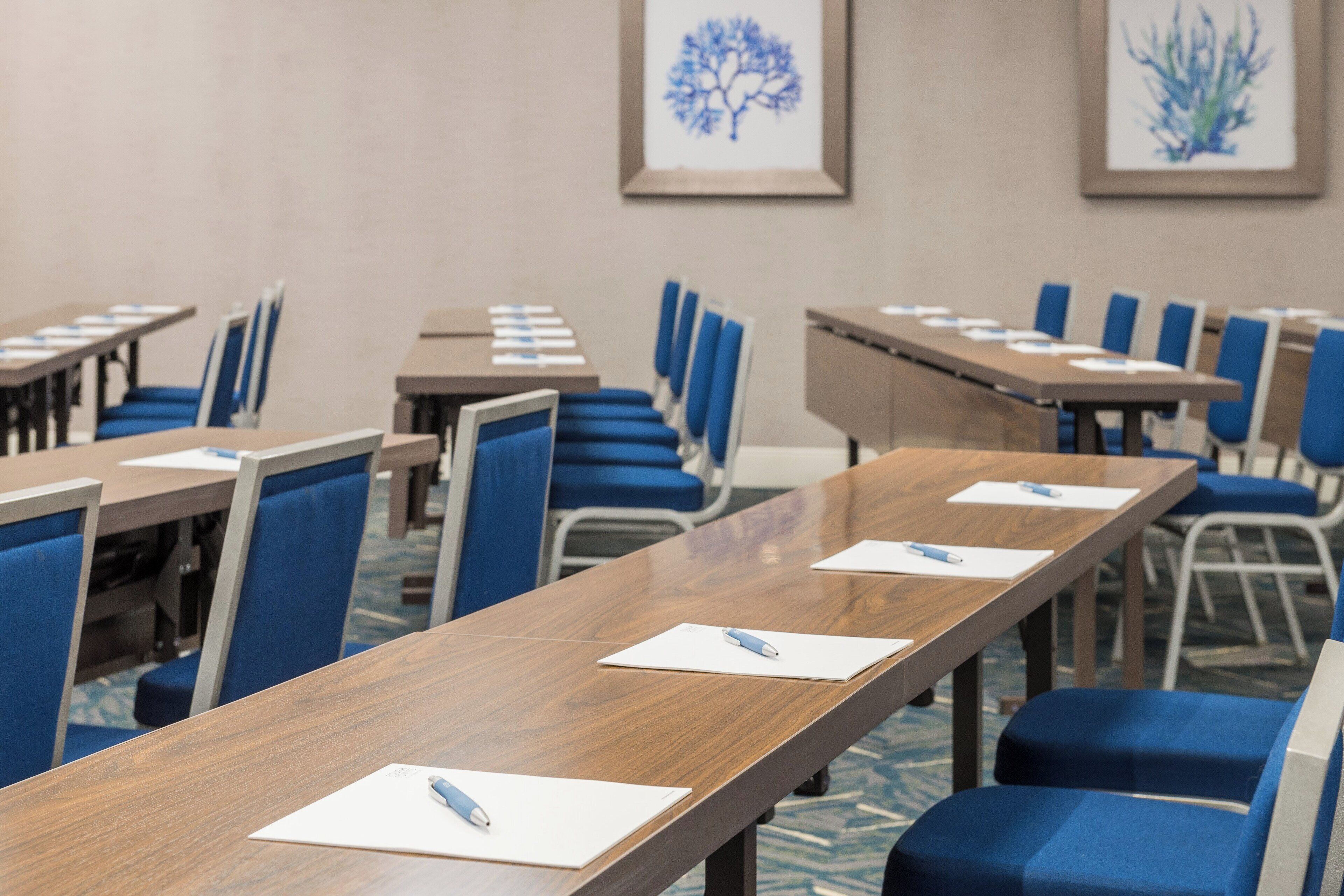 Un salón de conferencias con mesas largas, sillas azules y cuadros en las paredes.