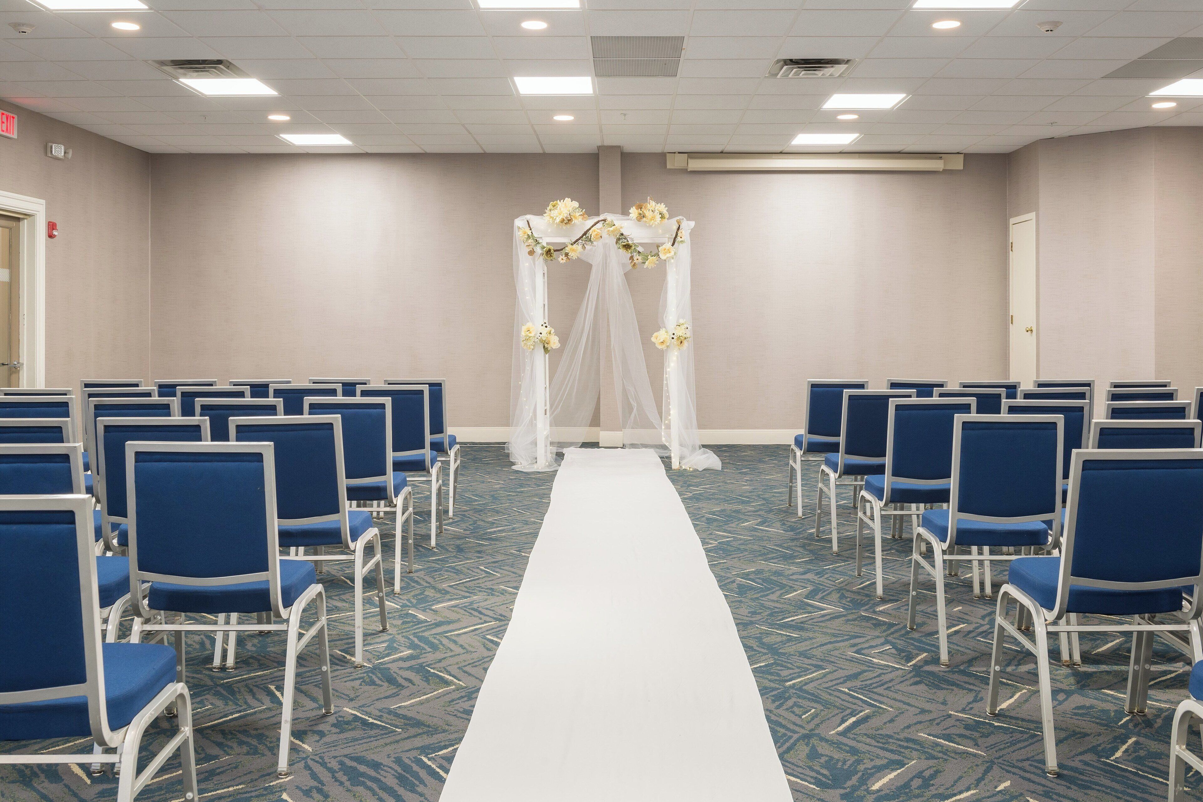 A hotel room with a long white carpet leading to a canopy with floral decorations.