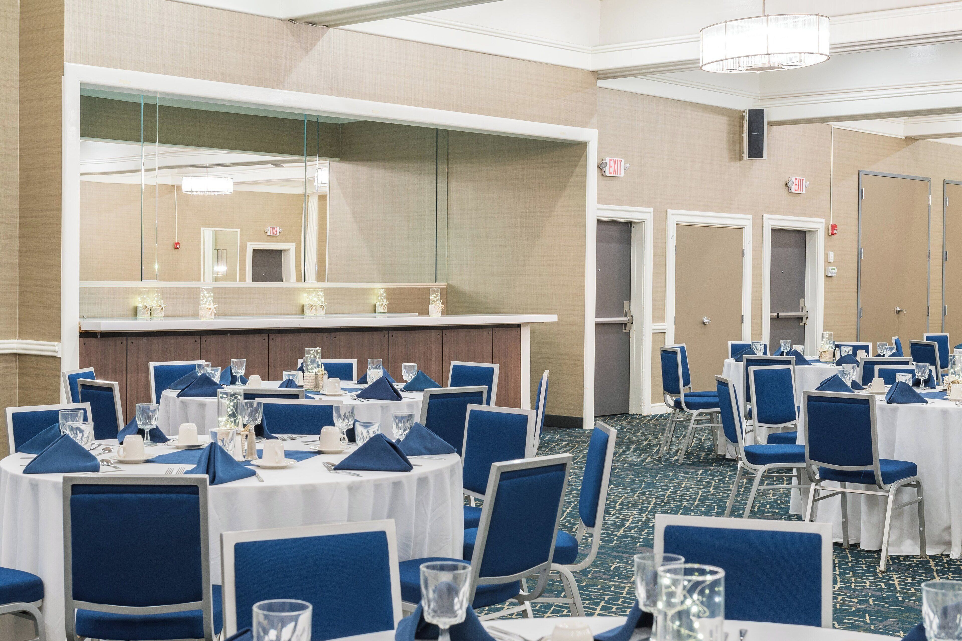 A banquet hall with round tables, blue chairs, and white tablecloths.