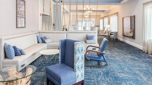A spacious lobby with a blue patterned carpet, a sofa with blue and white pillows, a glass coffee table, and a blue armchair. - Four Points by Sheraton Eastham Cape Cod (Eastham)