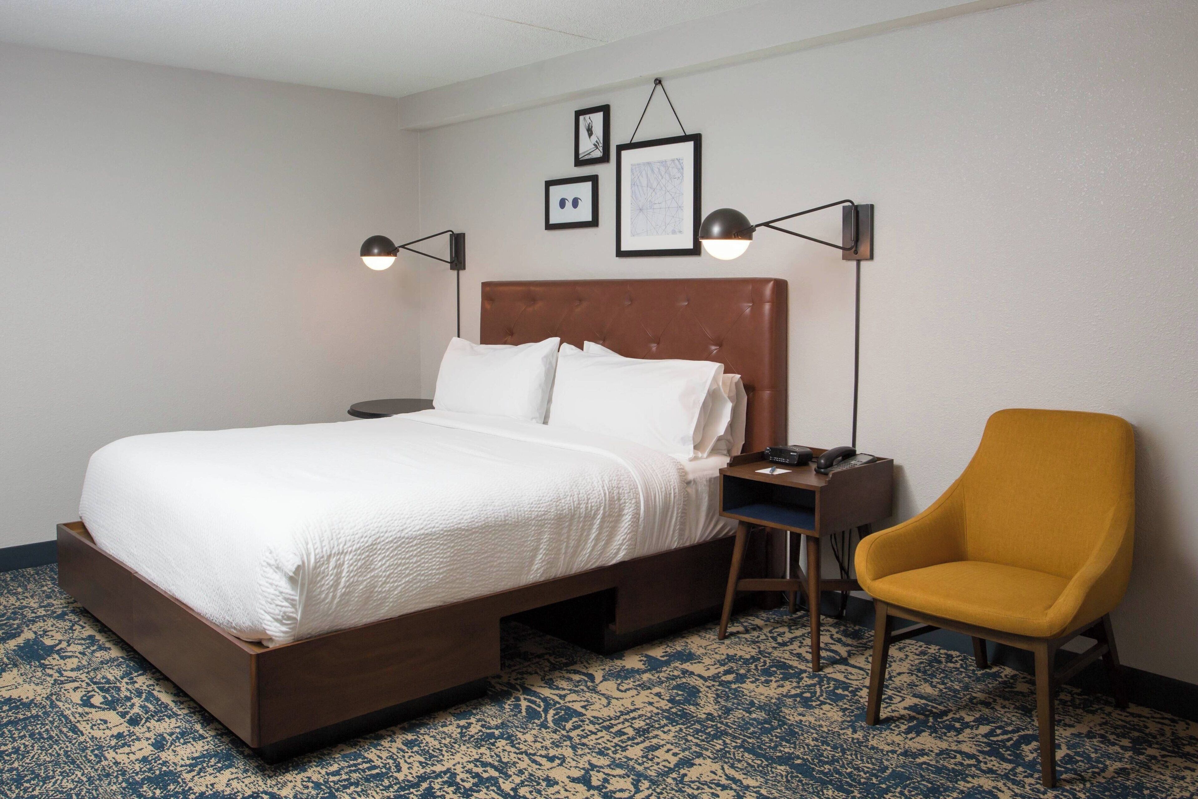 Ein Hotelzimmer mit einem großen Bett, einem Schreibtisch, einem Sessel und einer Wandlampe.