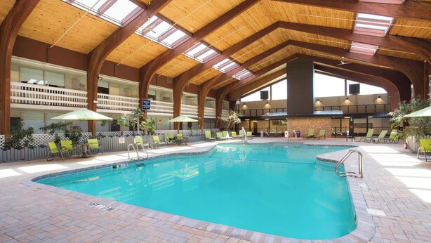 An indoor swimming pool with a wooden ceiling, multiple lounge chairs, and a brick floor. - Four Points by Sheraton Eastham Cape Cod (Eastham)
