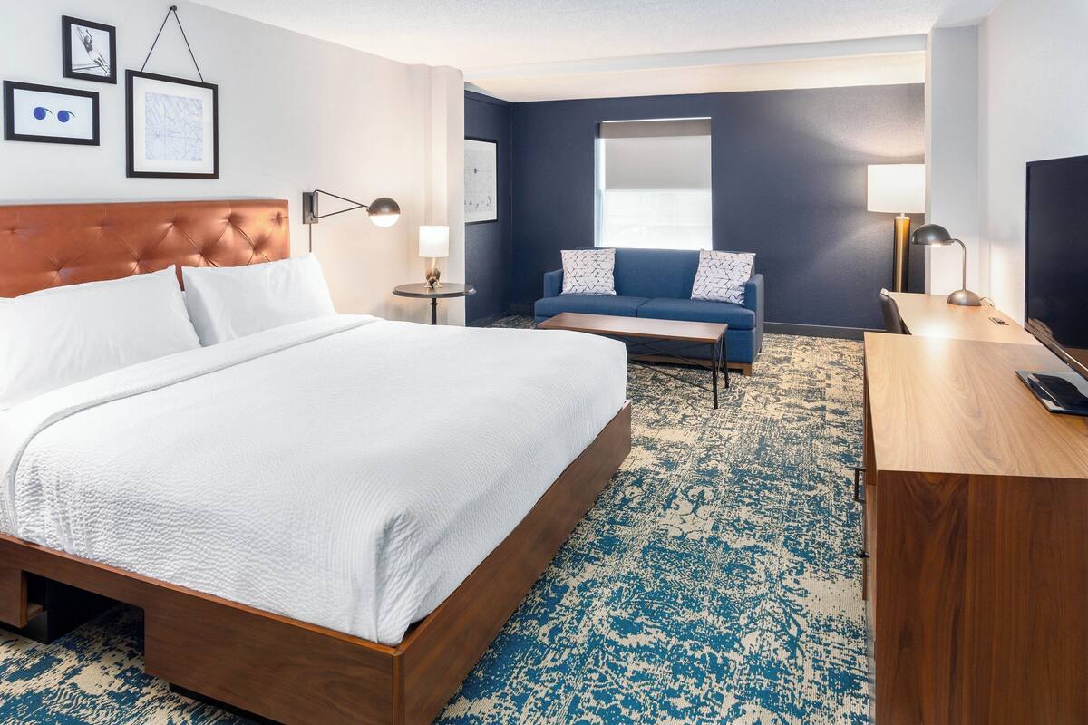 Una habitación de hotel con una cama grande, un sofá, un escritorio y un ventanal amplio.