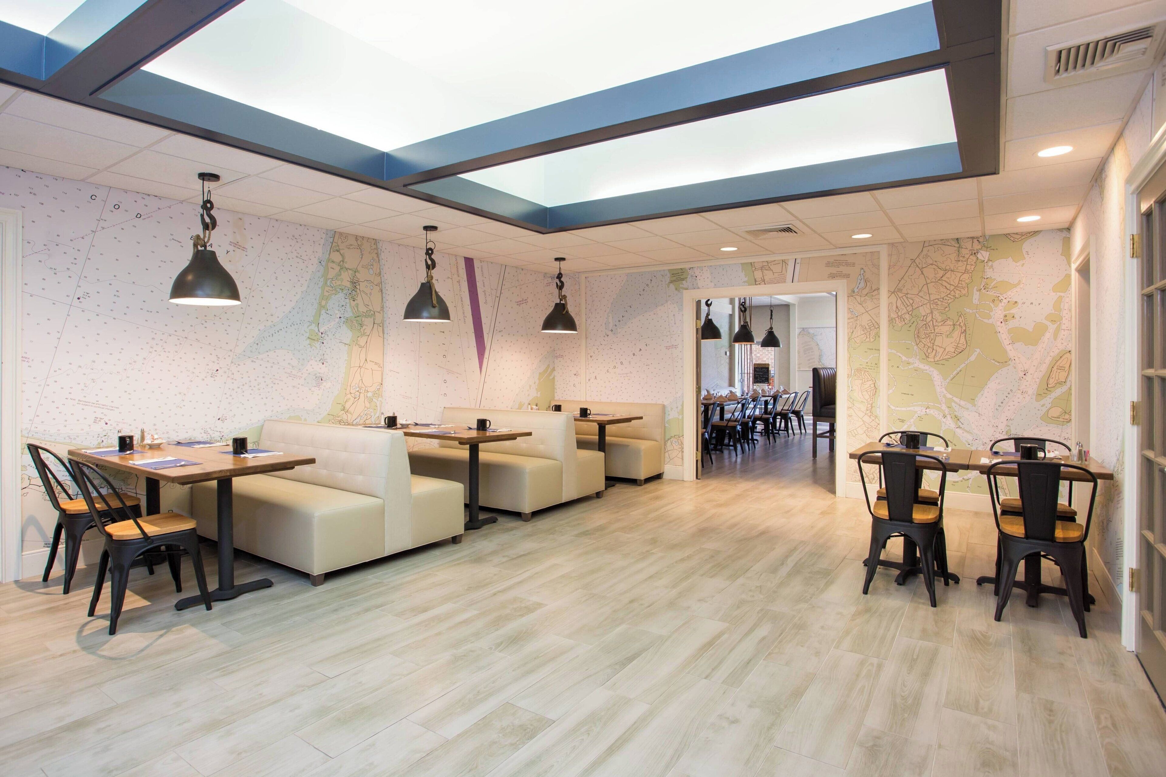 Un comedor moderno con techo alto, paredes con motivos de mapas y una variedad de opciones de asientos, incluyendo mesas y sofás.