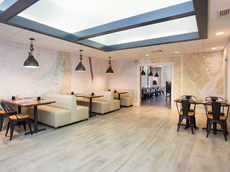 Un comedor moderno con techo alto, paredes con motivos de mapas y una variedad de opciones de asientos, incluyendo mesas y sofás.