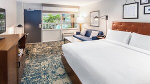 A hotel room with a bed, a desk, a sofa, a window with a view of a pool, and framed pictures on the wall. - Four Points by Sheraton Eastham Cape Cod (Eastham)