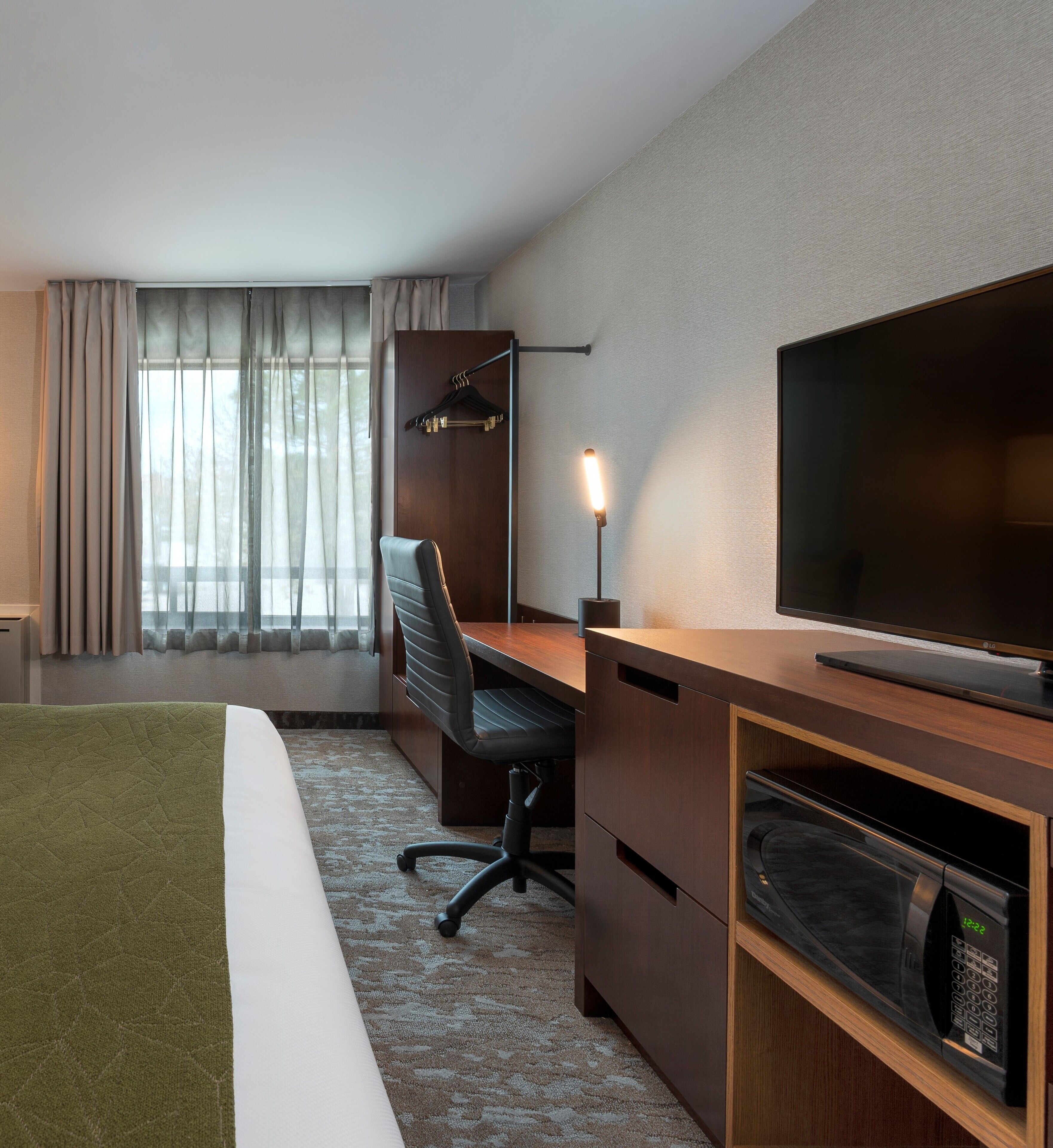 A hotel room with a bed, a desk, a chair, a television, and a microwave.