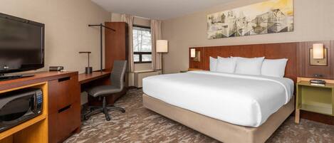 A hotel room with a large bed, a desk with a flat-screen TV, a microwave, and a chair.